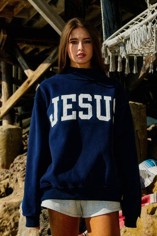 Person wearing a navy blue sweatshirt with 'JESUS' printed on it, standing in an outdoor setting.