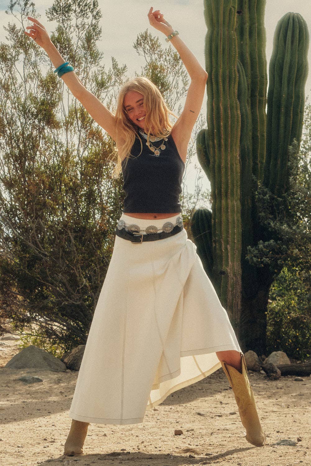 Woman in a desert setting with cacti, arms raised