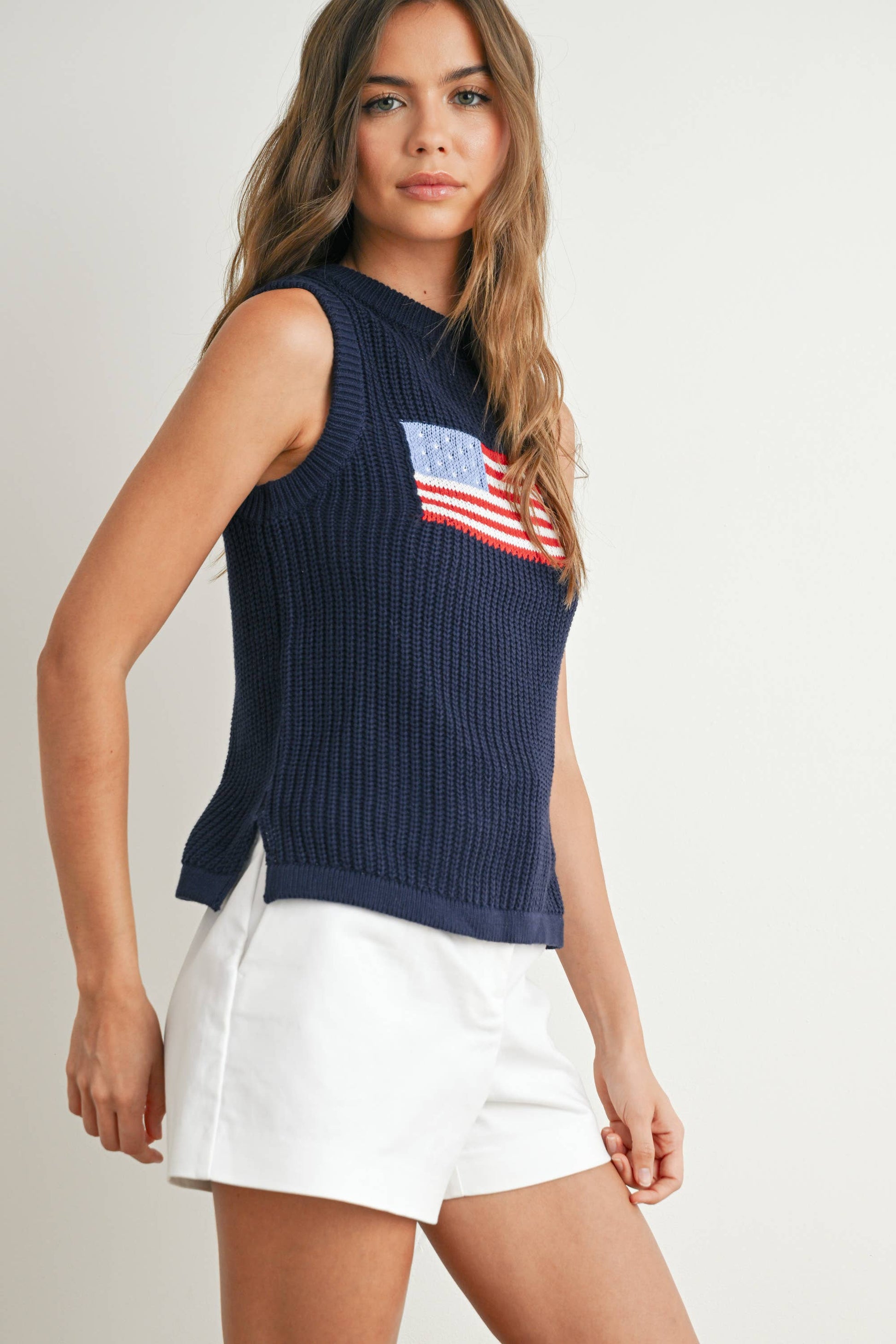 Woman wearing a navy sleeveless sweater with an American flag design on a plain background
