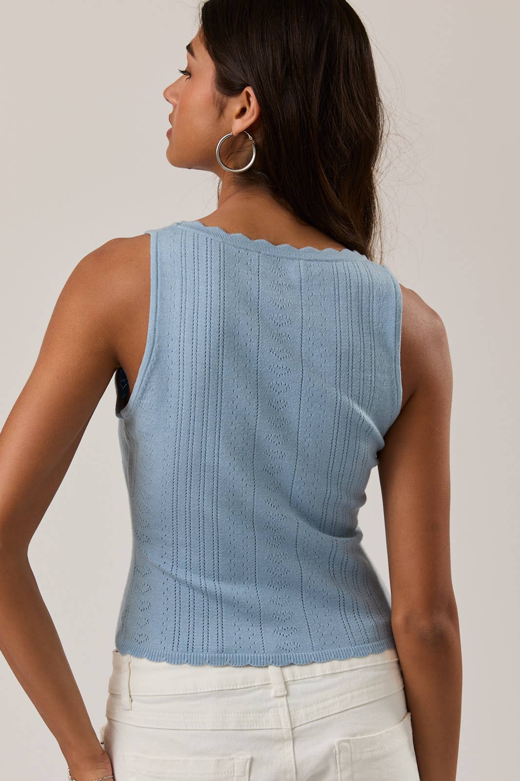 Woman wearing a light blue sleeveless top with a plain background