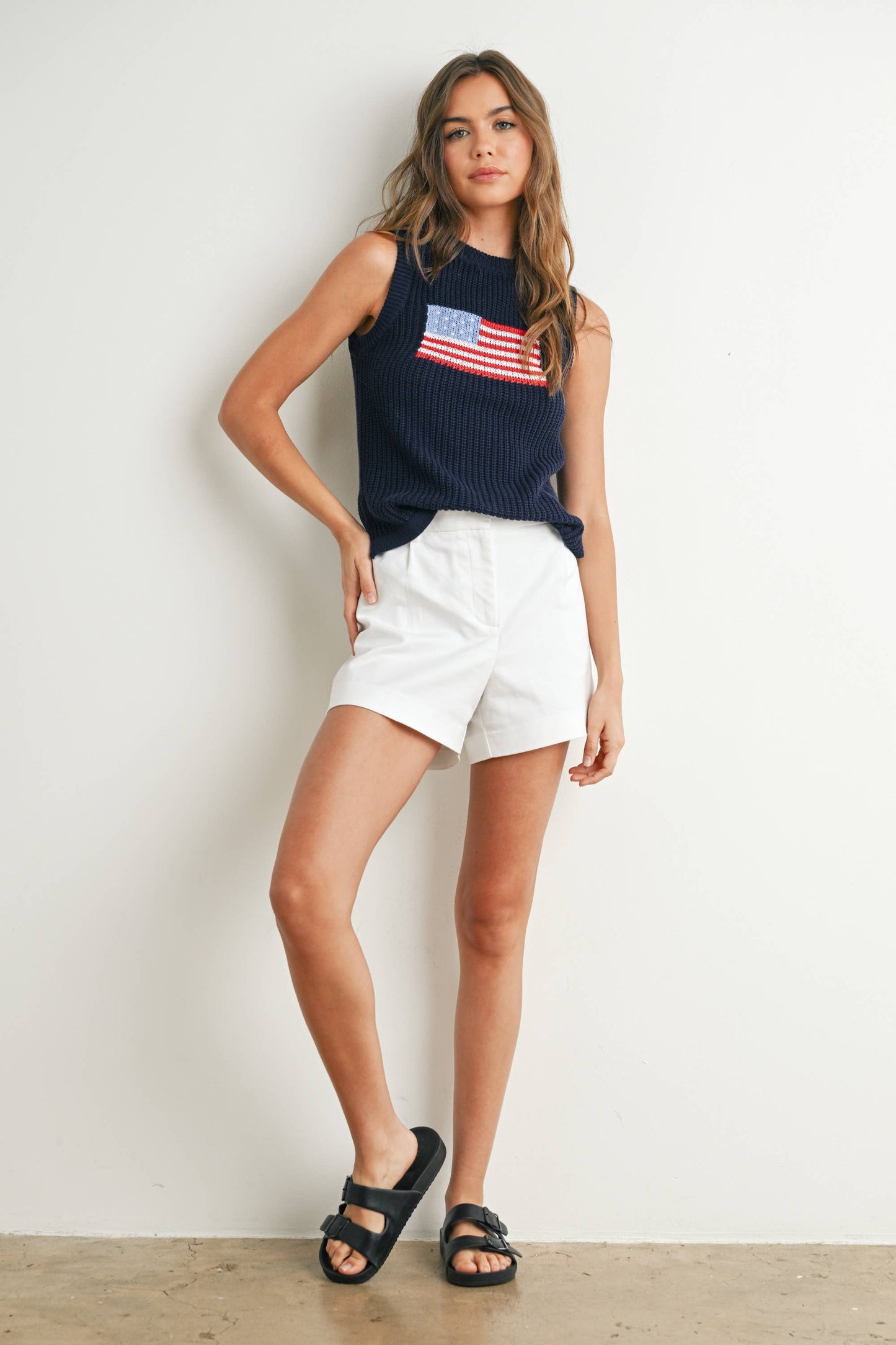Woman wearing a navy sleeveless top with an American flag design and white shorts against a plain background