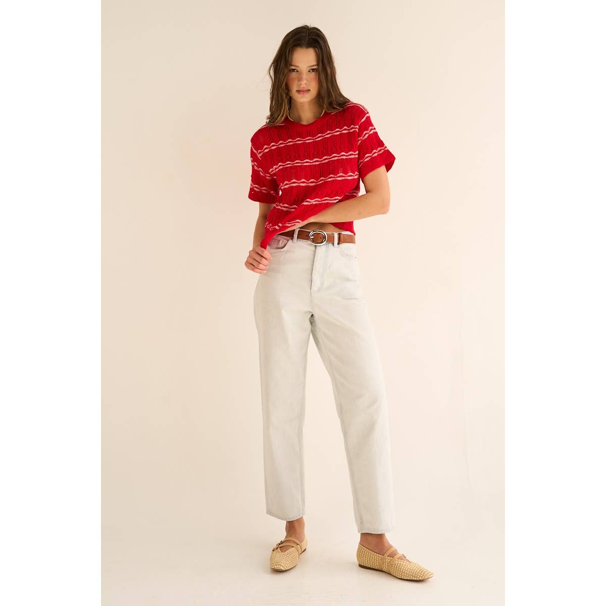 Woman wearing a red striped shirt and white pants on a beige background