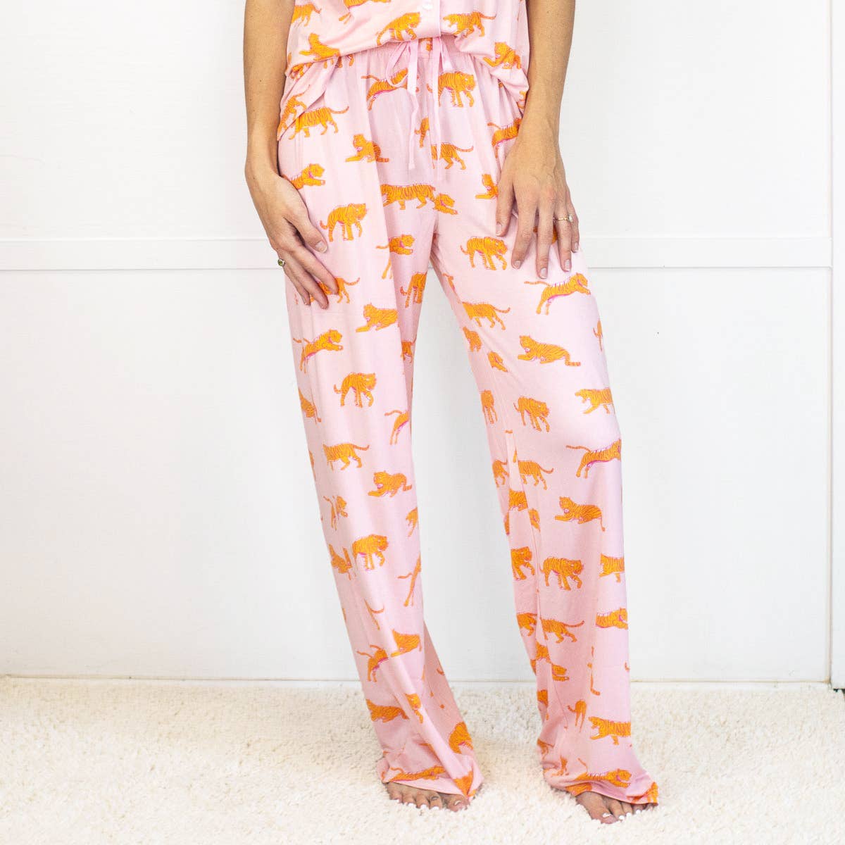 Pink pajama pants with orange panther pattern worn by a person on a white background