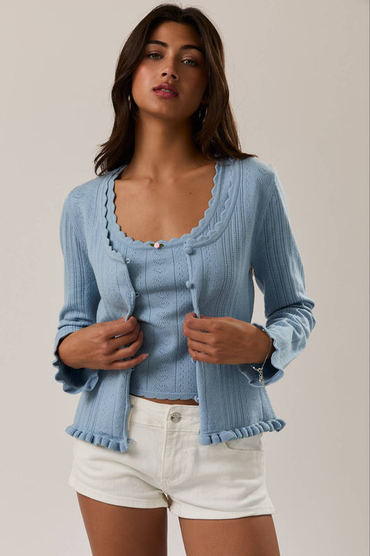 Woman wearing a light blue cardigan over a top and white shorts on a plain background