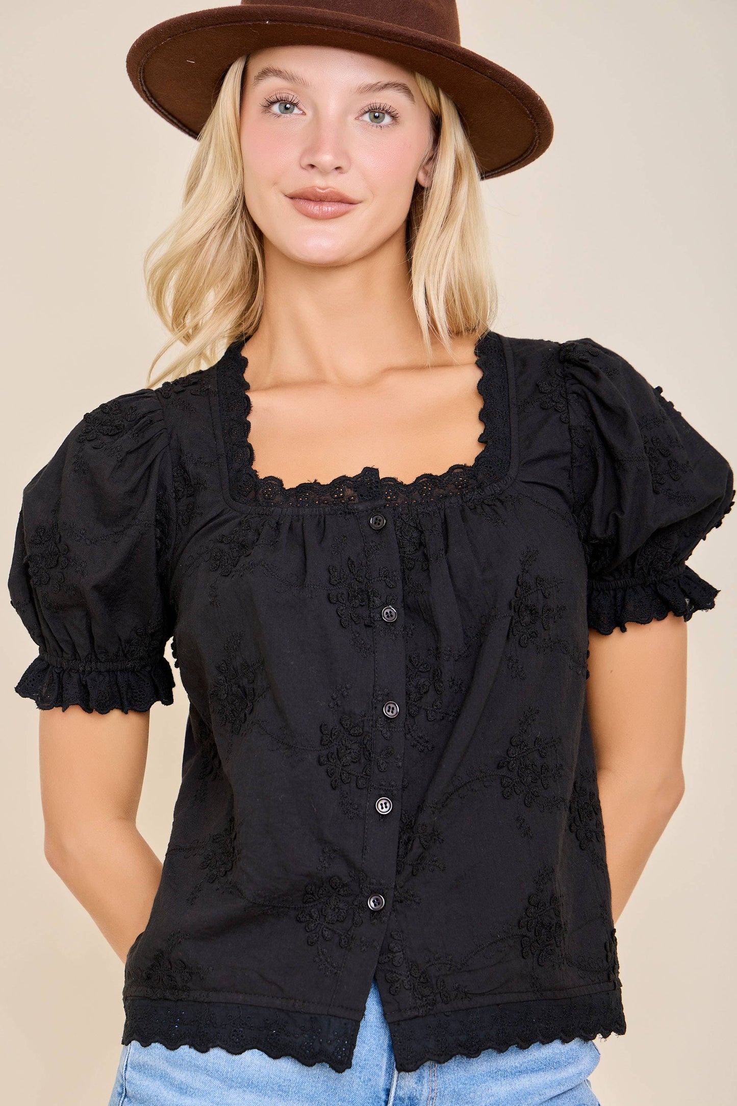 Woman wearing a black blouse with ruffled sleeves and a brown hat on a beige background