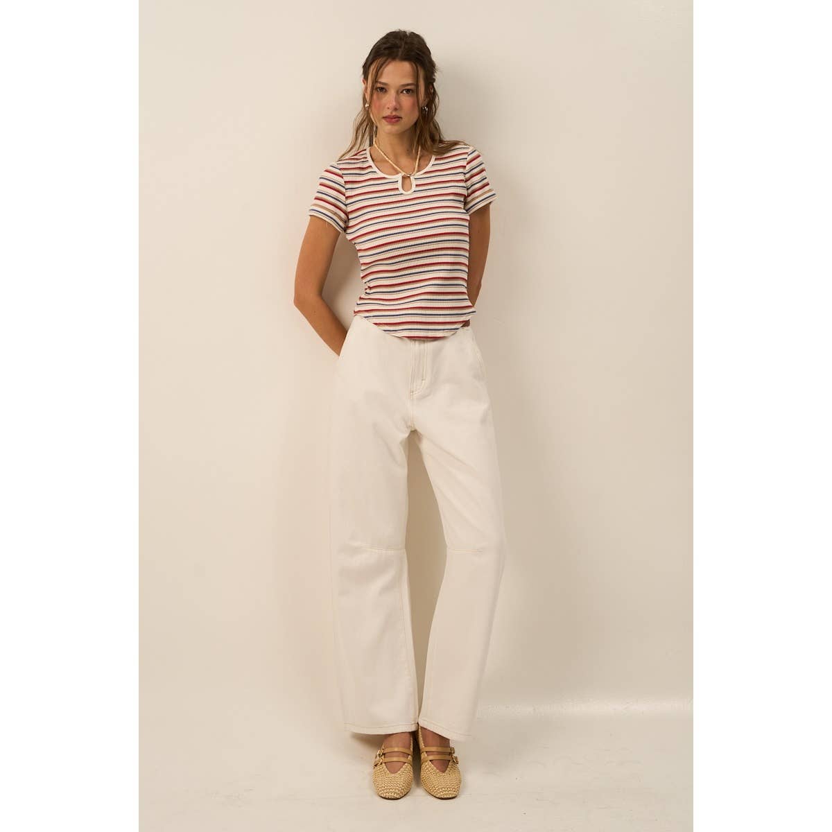 Woman wearing a striped shirt and white pants against a plain background