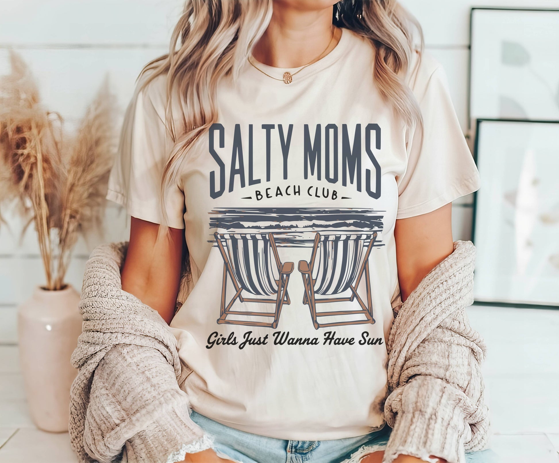 Person wearing a 'Salty Moms Beach Club' t-shirt with lounge chairs graphic.
