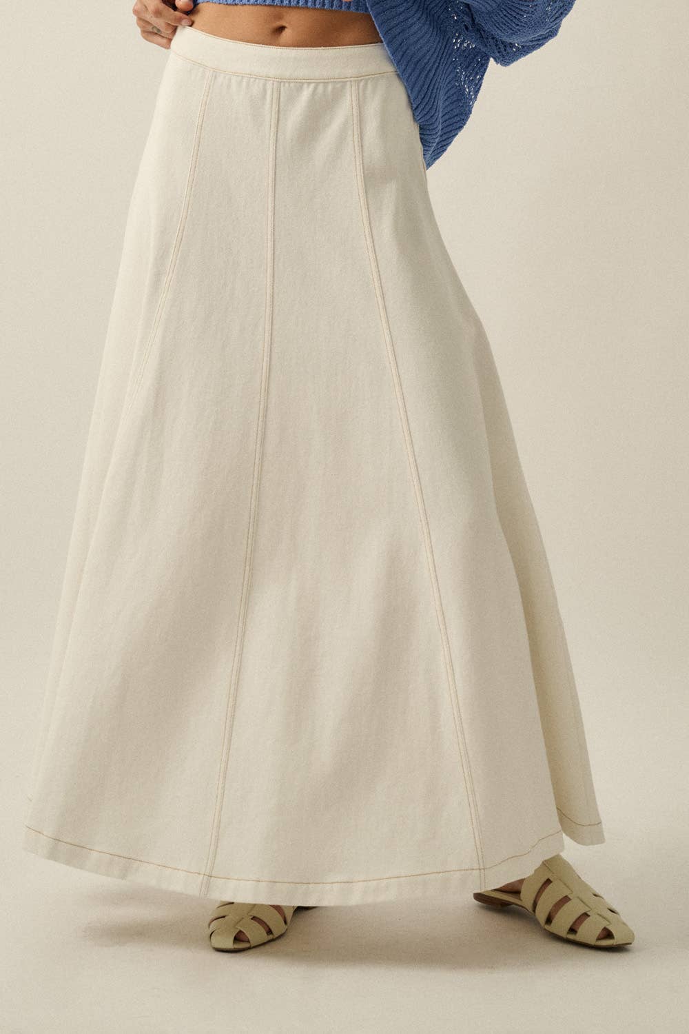 Person wearing a long beige skirt on a plain background