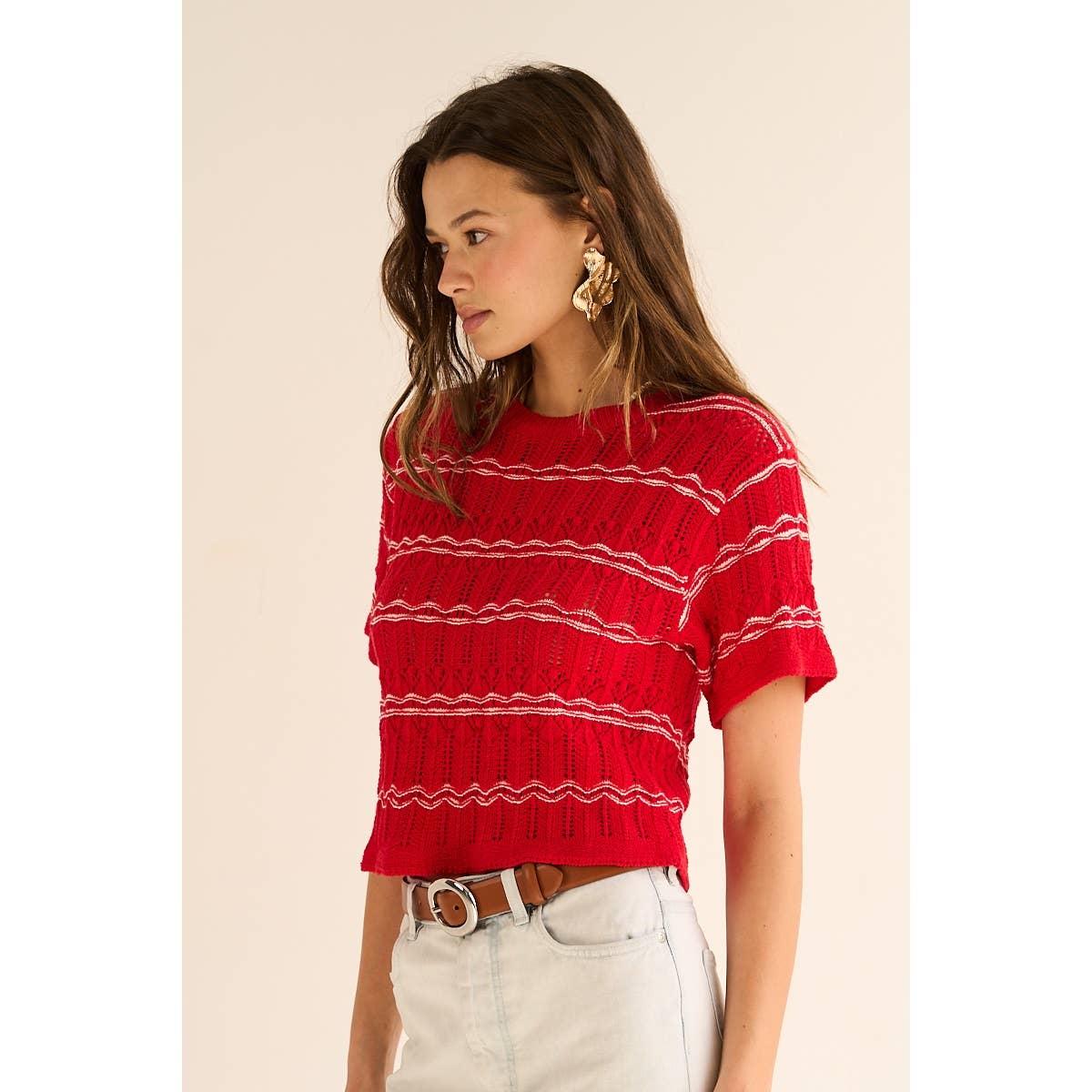 Woman wearing a red striped sweater and white pants against a beige background