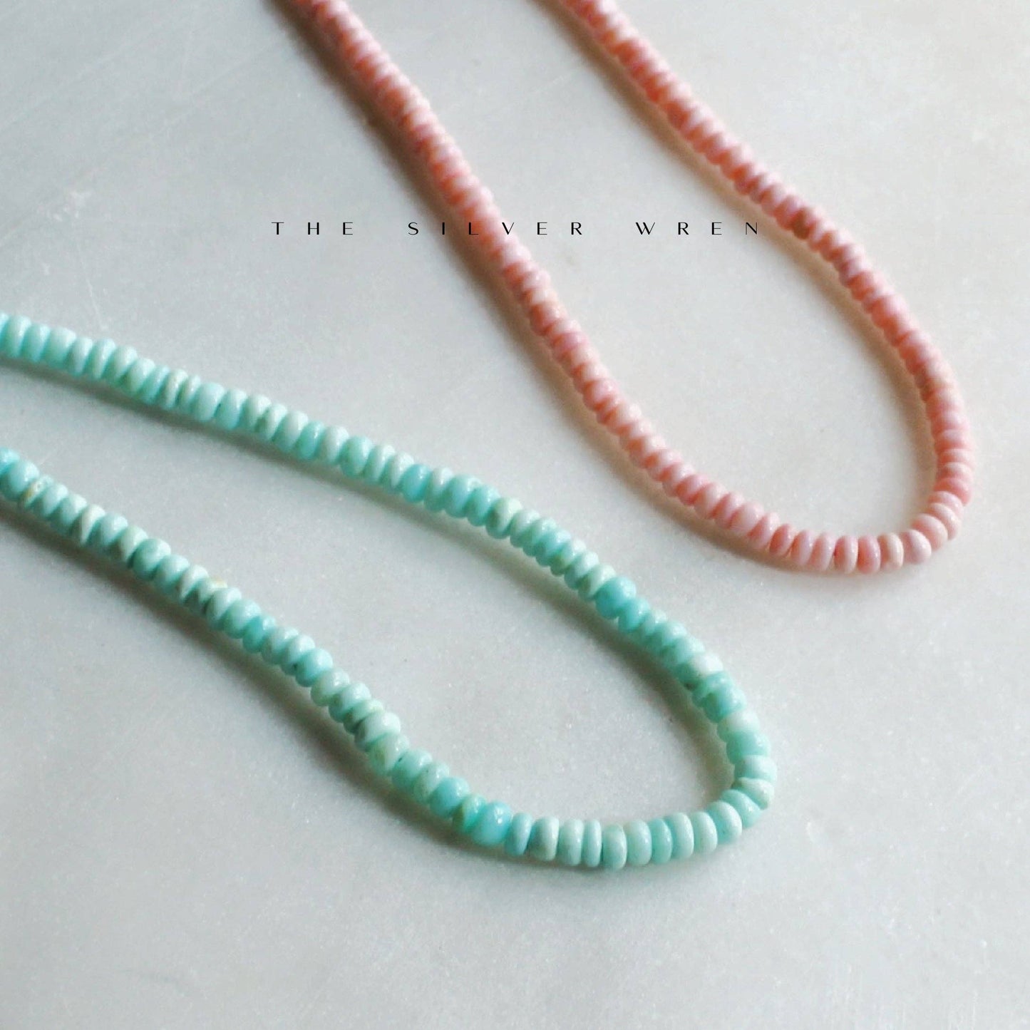 Aqua and pink beaded necklace strands on pale stone surface