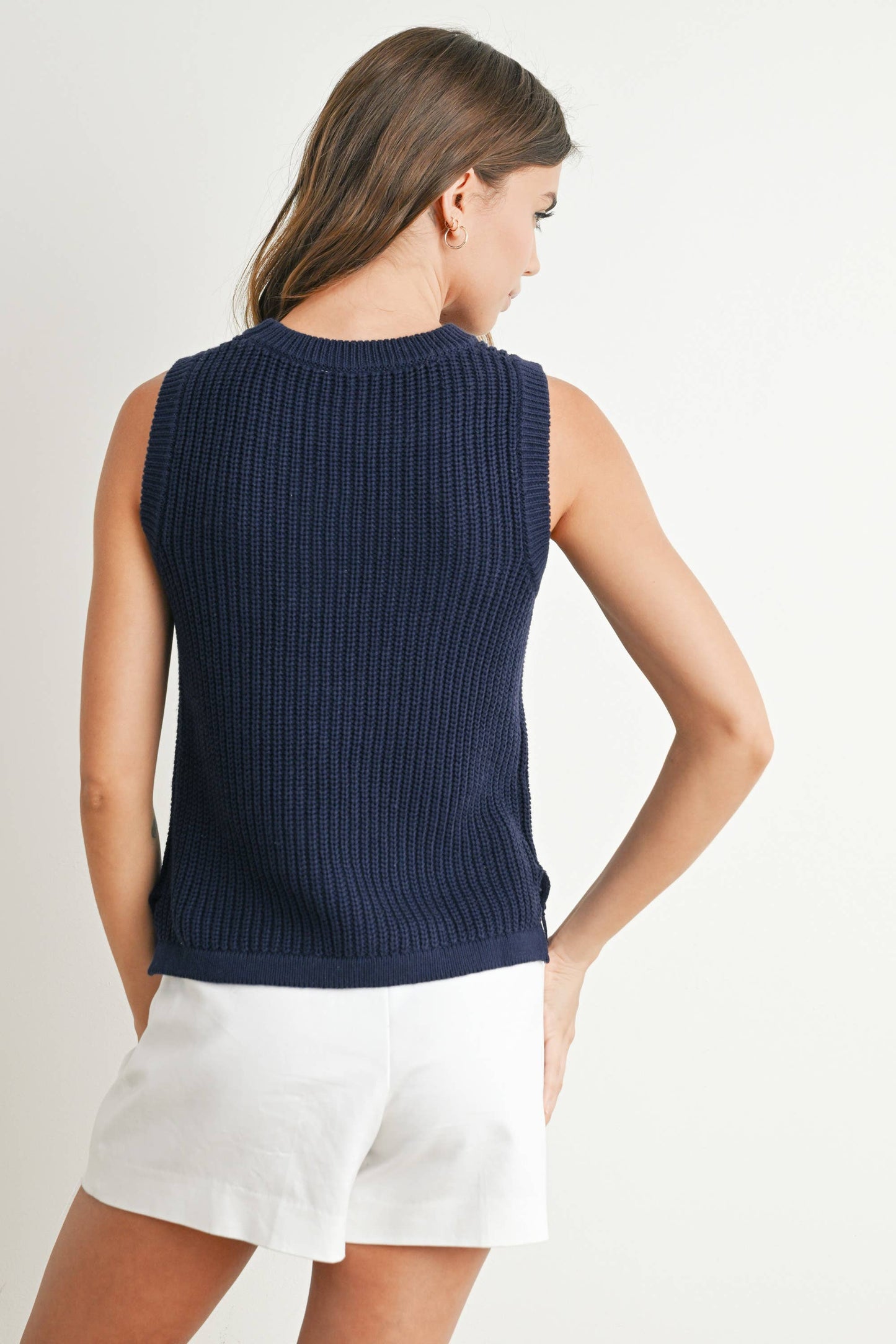 Woman wearing a navy sleeveless sweater over a white top with a light background