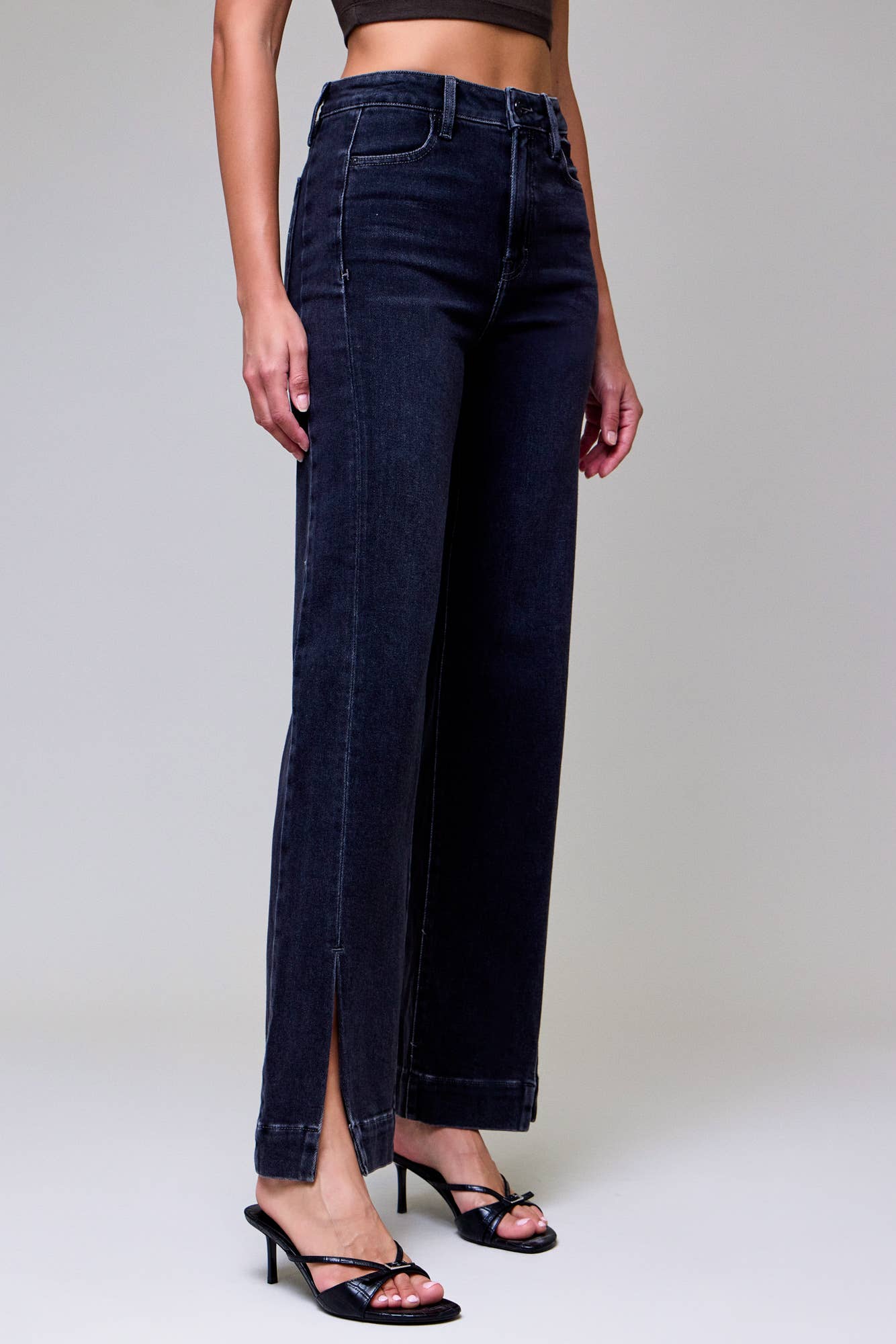 Person wearing dark blue jeans with a high slit on a plain background