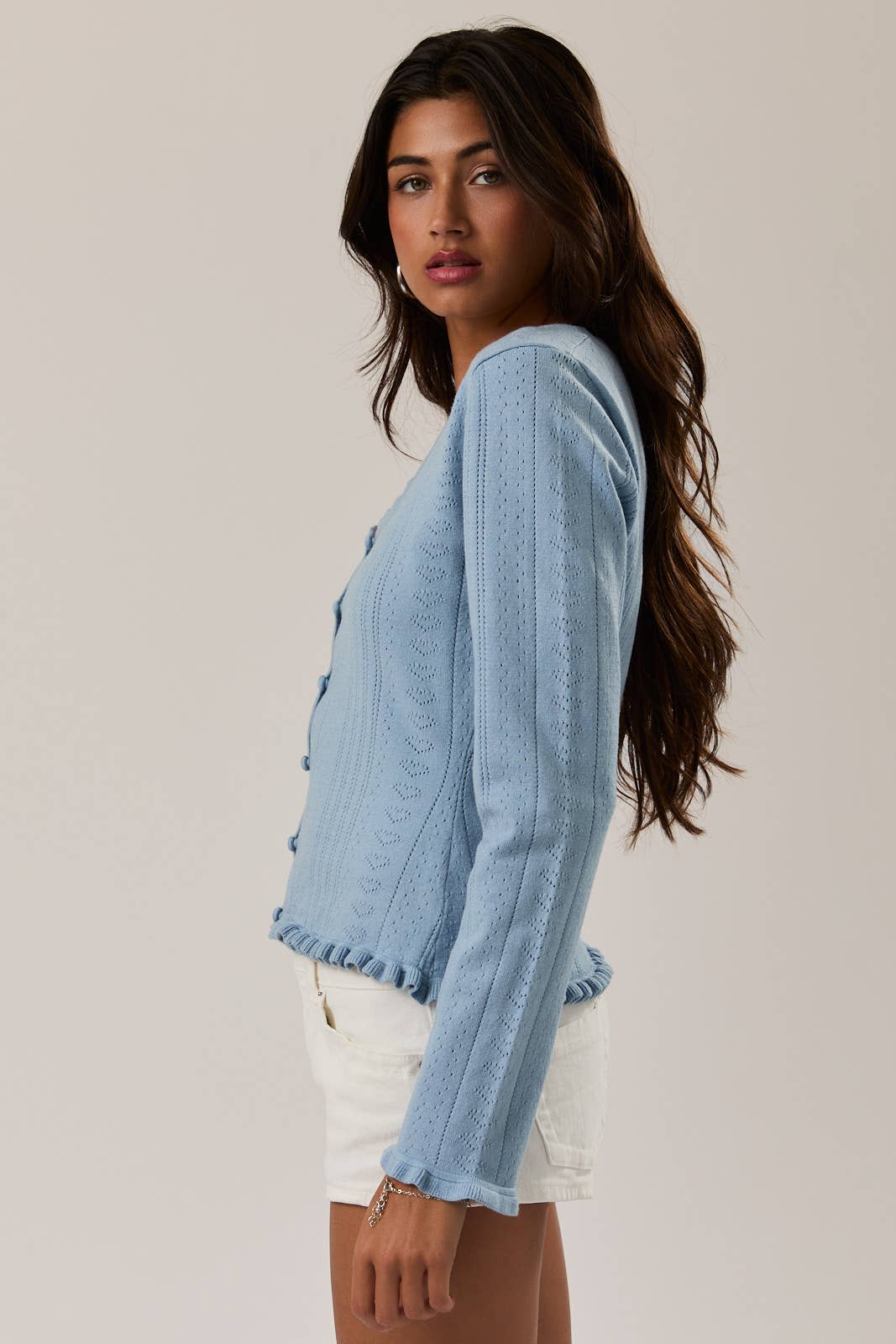 Woman wearing a light blue cardigan over a white top on a plain background