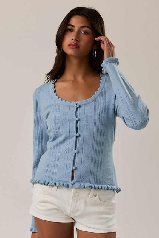 Woman wearing a light blue ribbed sweater and white shorts against a neutral background