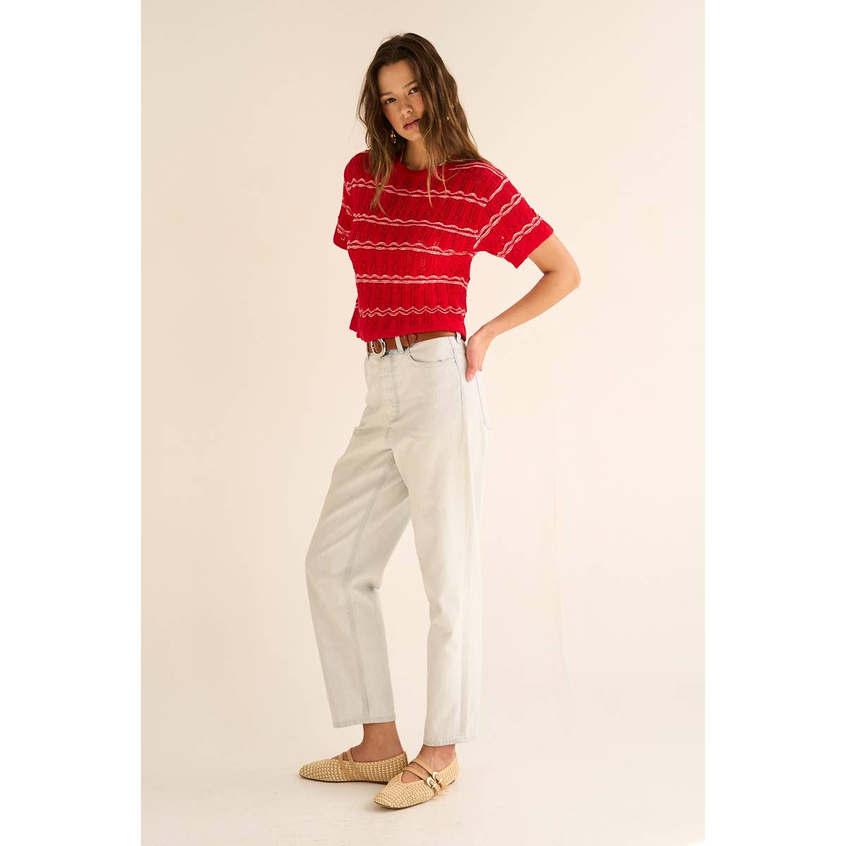 Woman wearing a red sweater with white stripes and white pants on a beige background