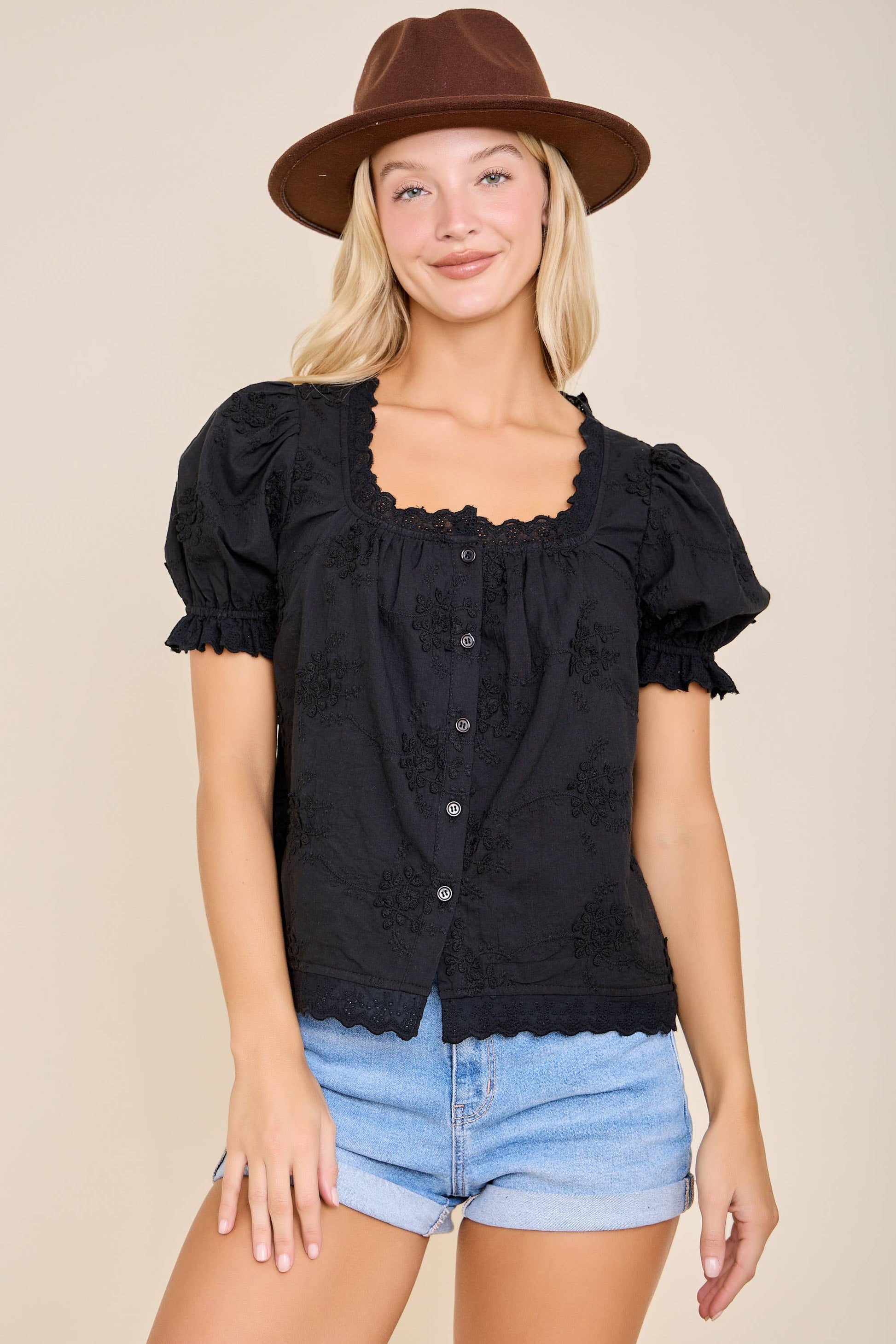Woman wearing a black top with ruffled sleeves and denim shorts on a beige background