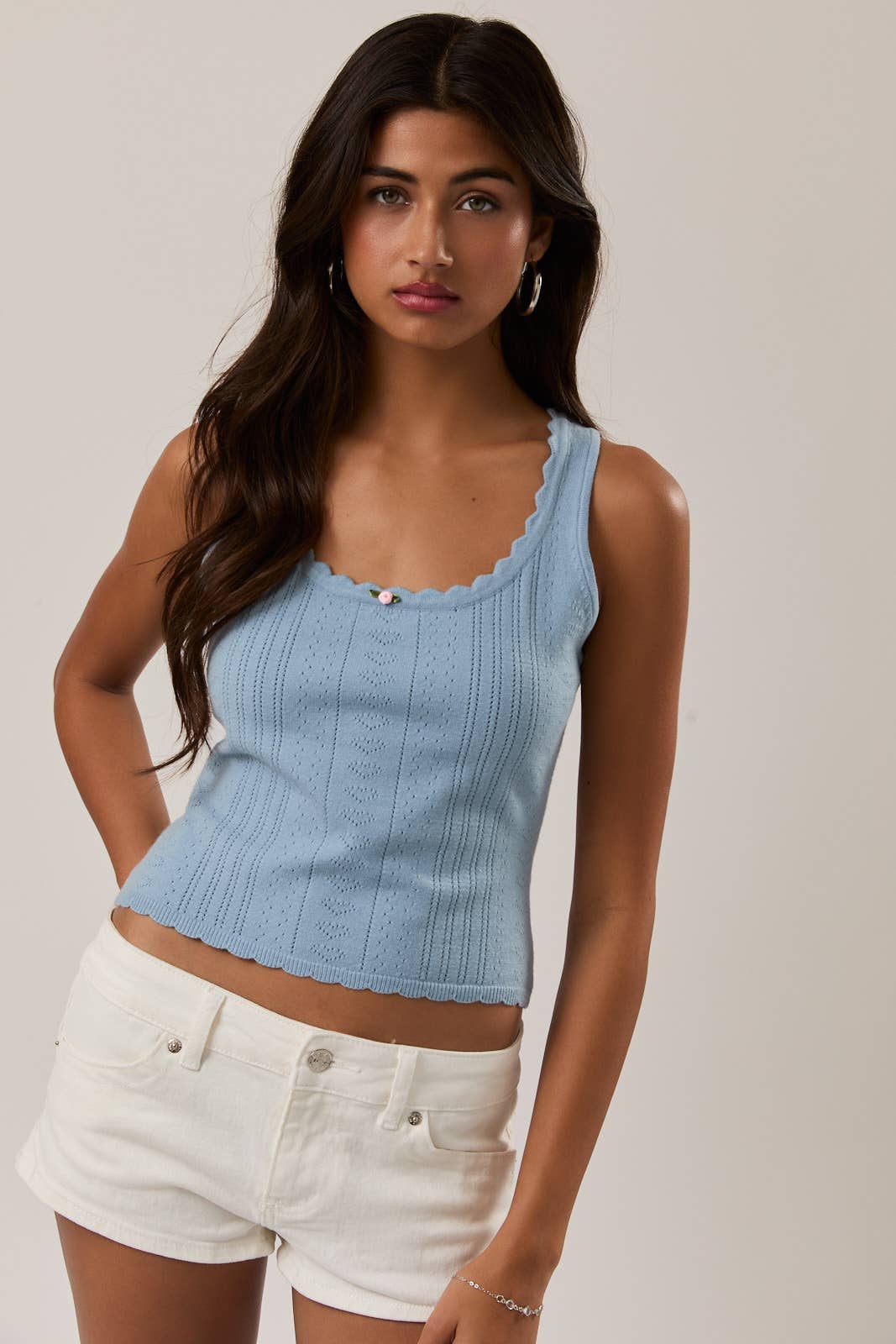 Woman wearing a light blue sleeveless top and white shorts on a plain background
