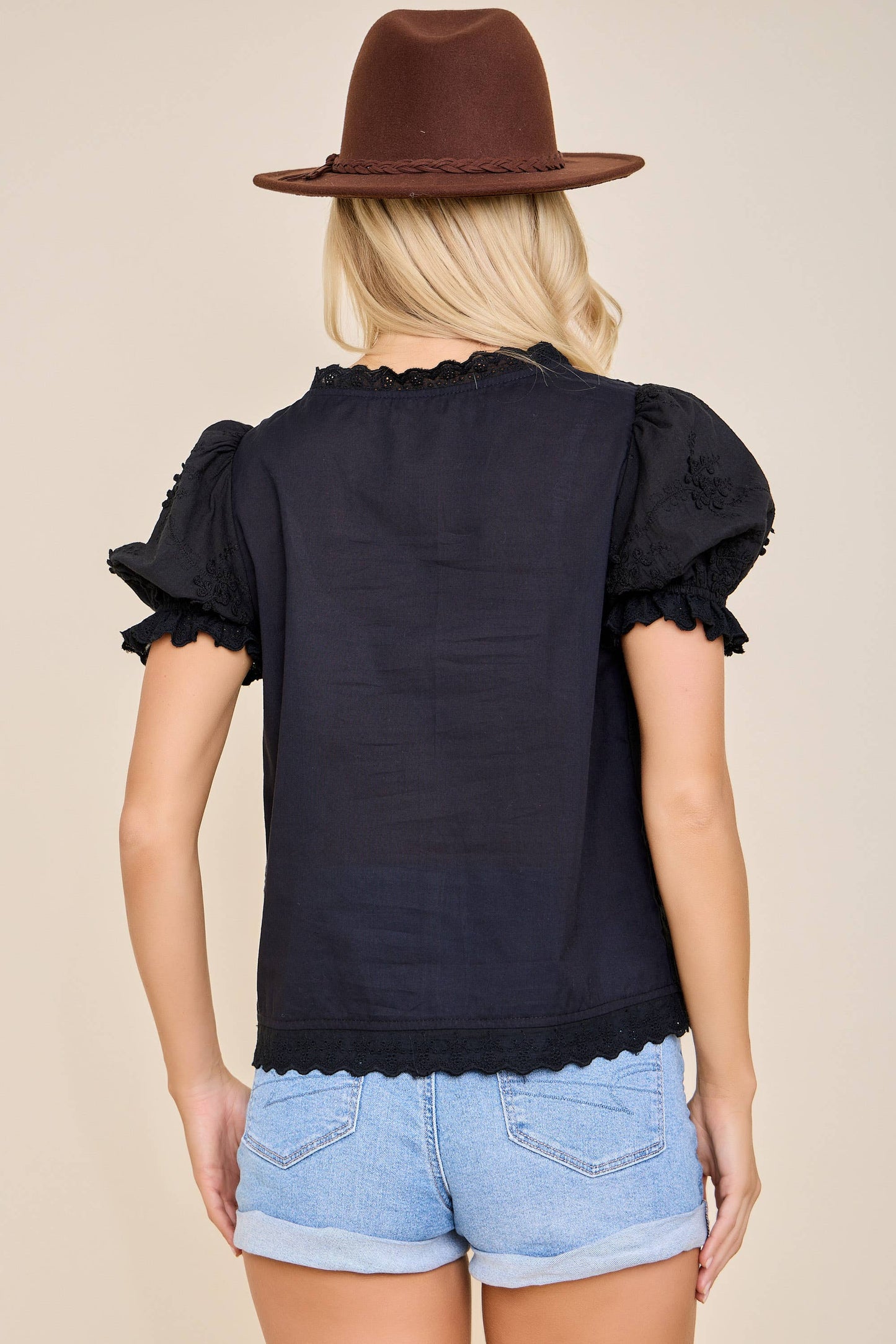 Person wearing a black top with ruffled sleeves and denim shorts on a beige background