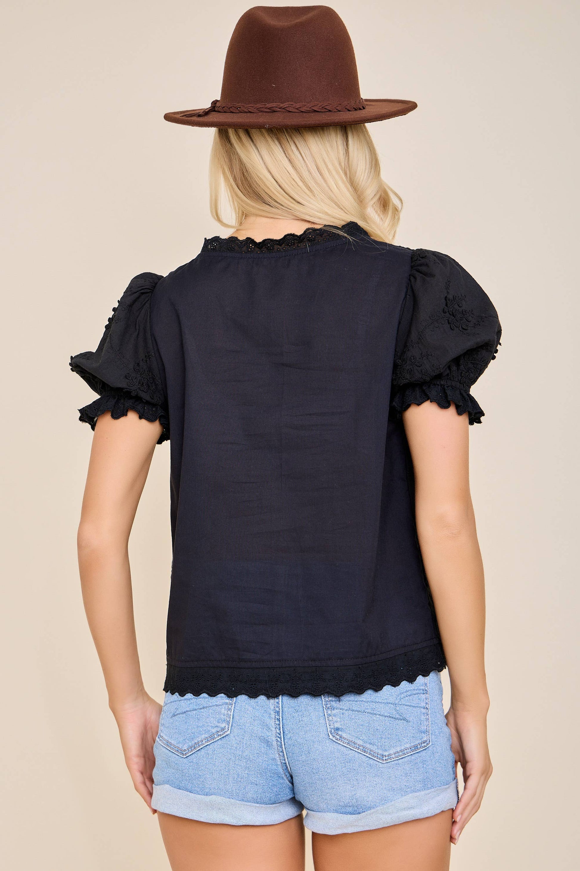 Person wearing a black top with ruffled sleeves and denim shorts on a beige background