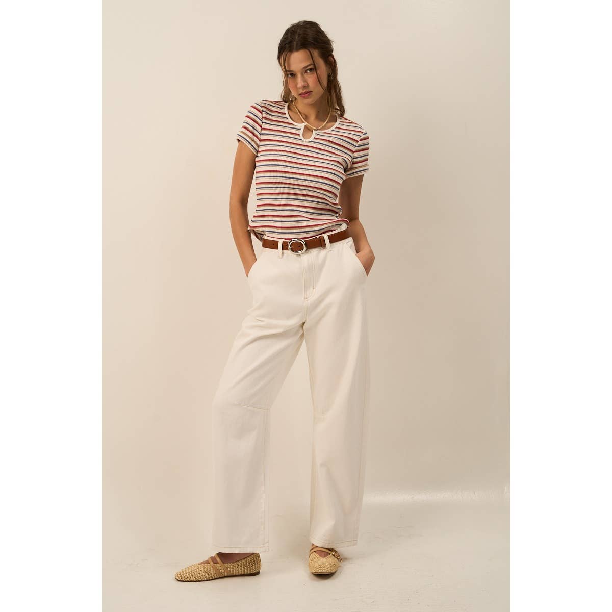 Woman wearing a striped shirt and white pants against a plain background