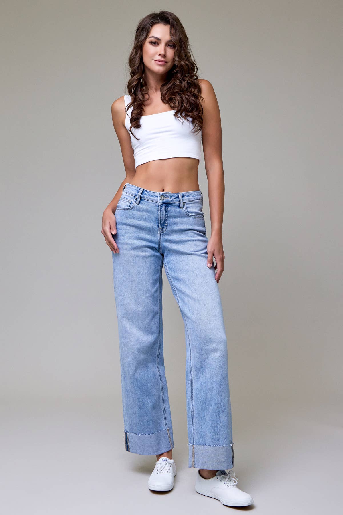 Woman wearing light blue jeans and a white top on a plain background