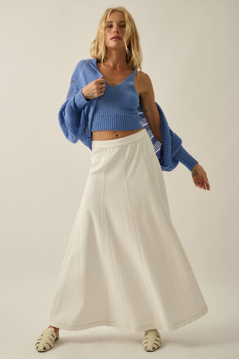 Woman wearing a blue sweater and white pants on a plain background