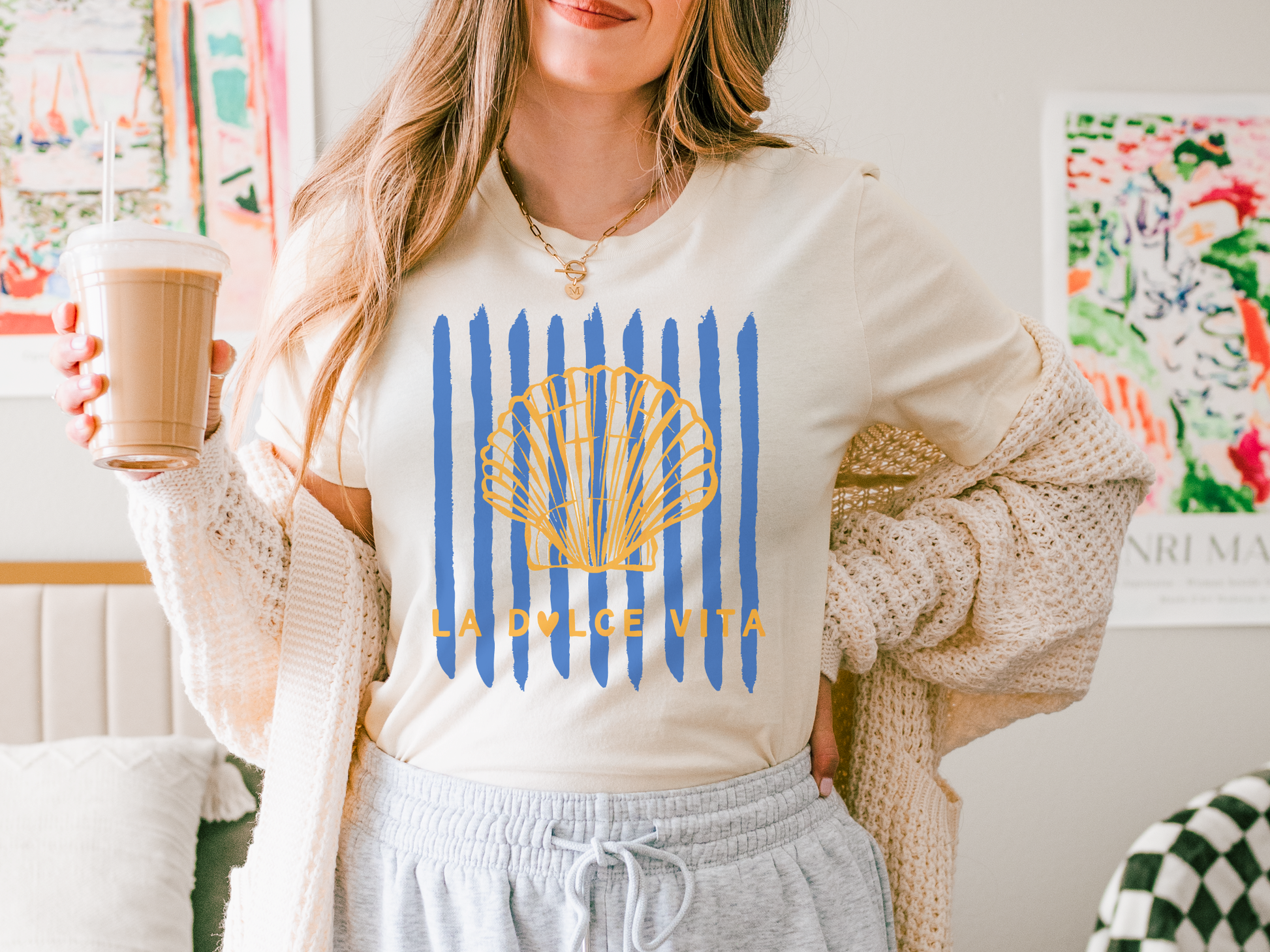 Woman wearing a 'La Dolce Vita' sweatshirt holding a coffee cup in a cozy room.