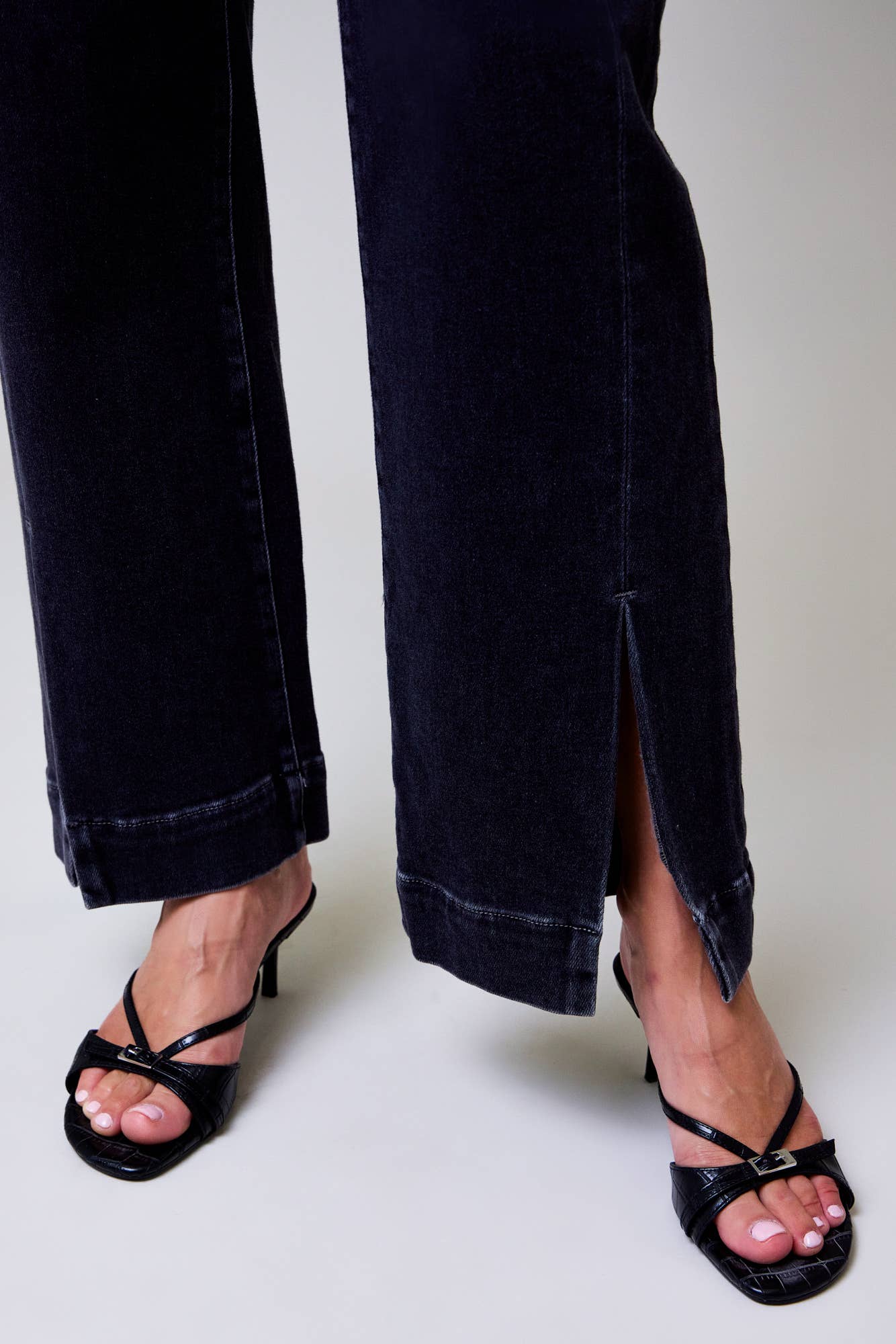 Person wearing black high-heeled sandals and dark jeans on a plain background