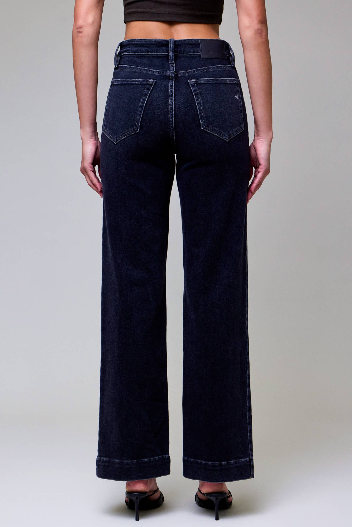 Person wearing dark blue jeans from behind on a plain background