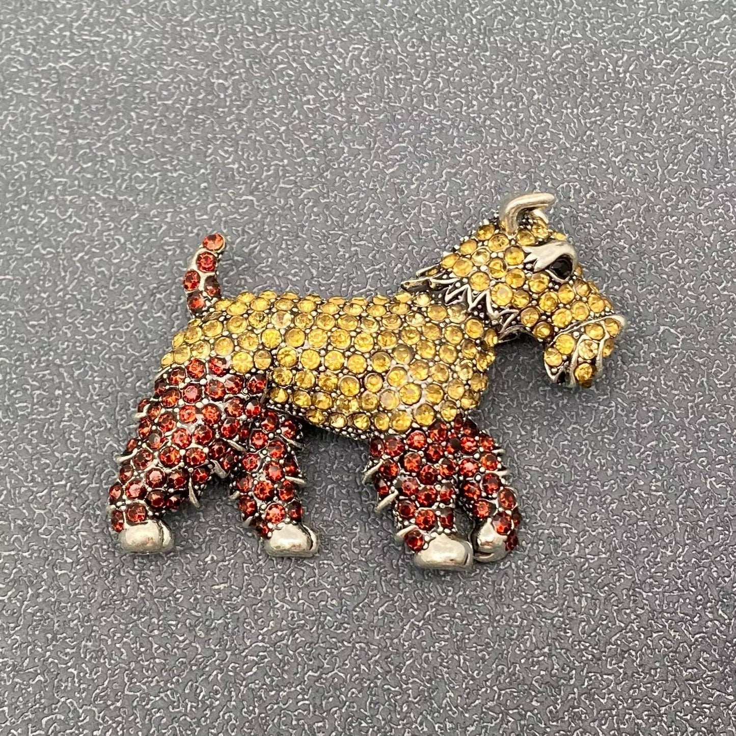 Dog-shaped brooch with yellow and red stones on a textured white background