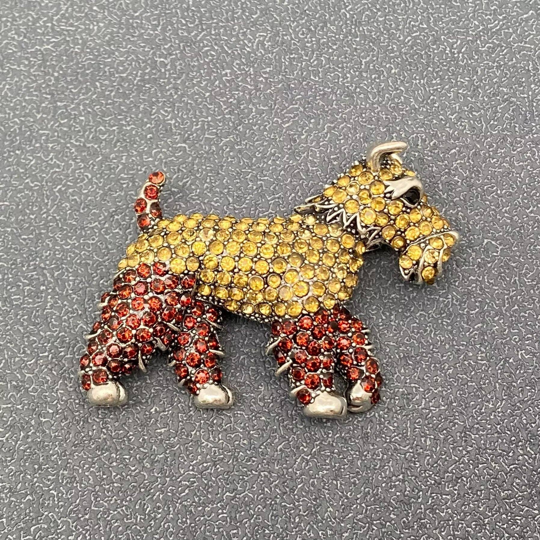 Dog-shaped brooch with yellow and red stones on a textured white background