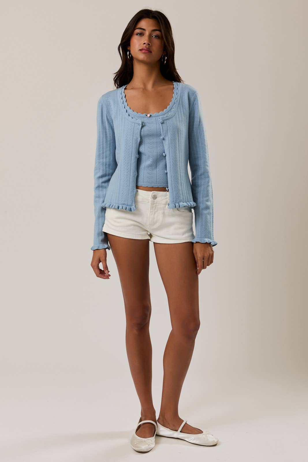 Woman wearing a light blue cardigan and white shorts on a plain background