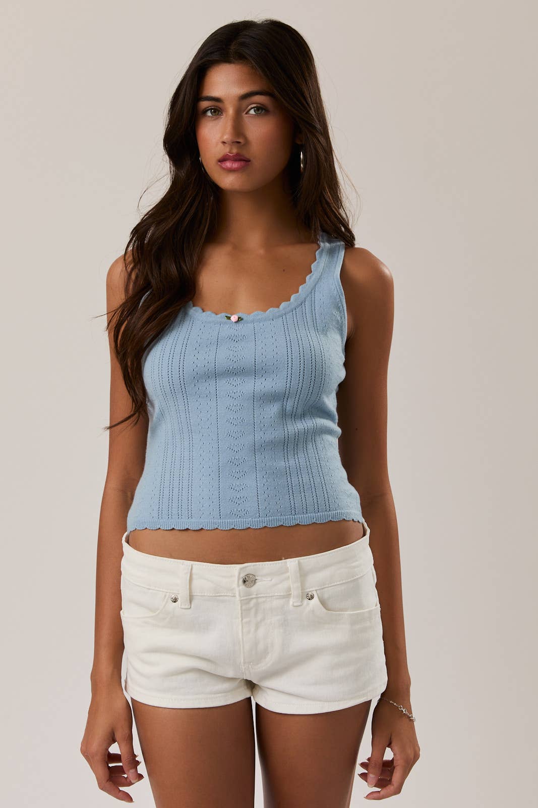 Woman wearing a light blue ribbed tank top and white shorts on a plain background