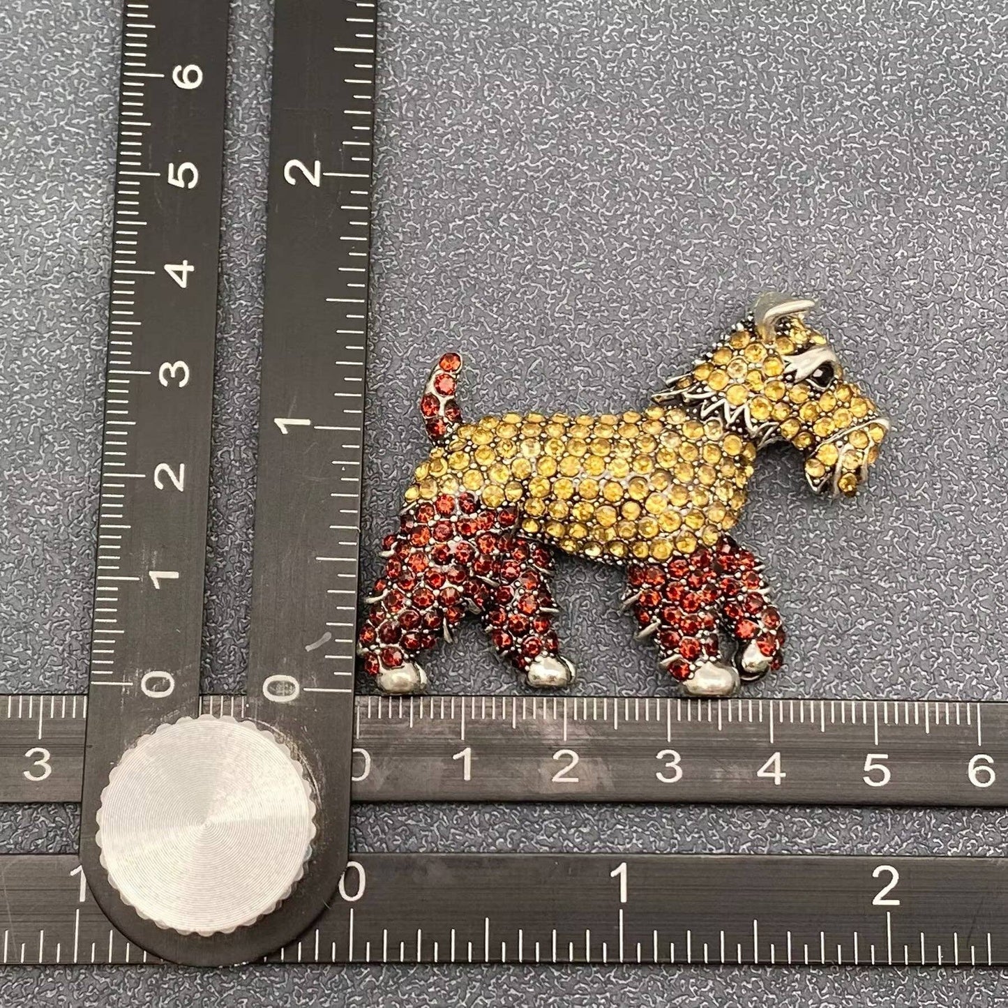 Dog-shaped brooch with gemstones on a gray background with a ruler for scale.