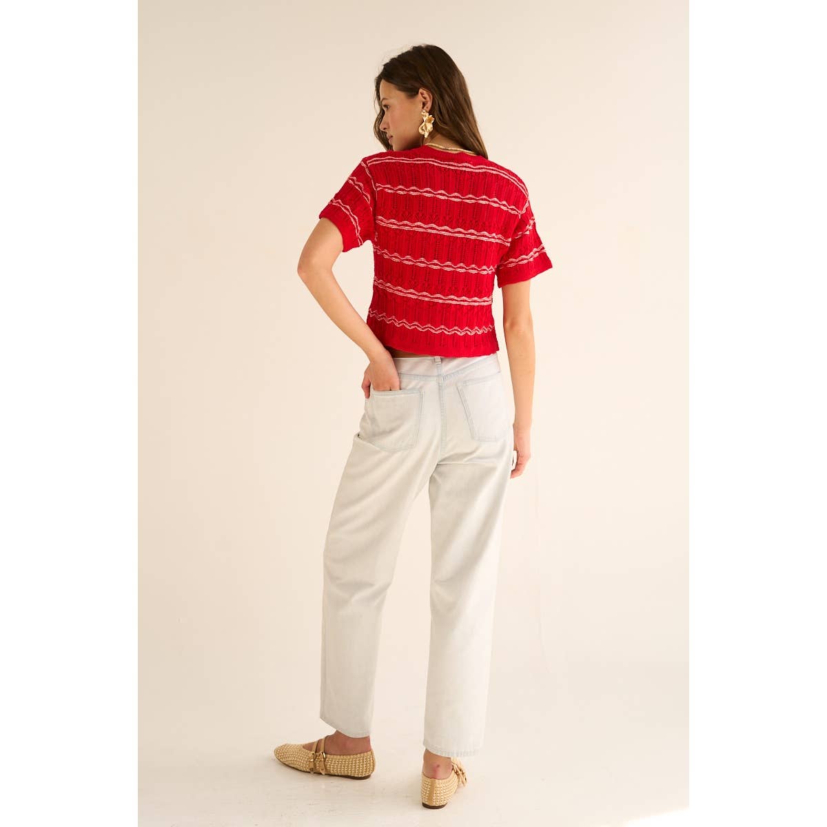 Woman wearing a red striped shirt and white pants on a beige background