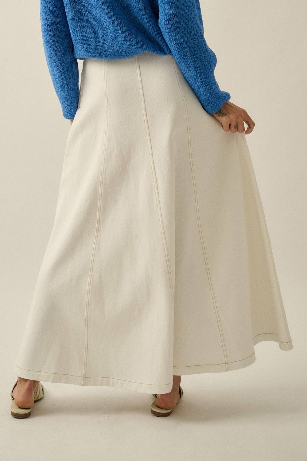 Person wearing a blue sweater and white skirt on a plain background
