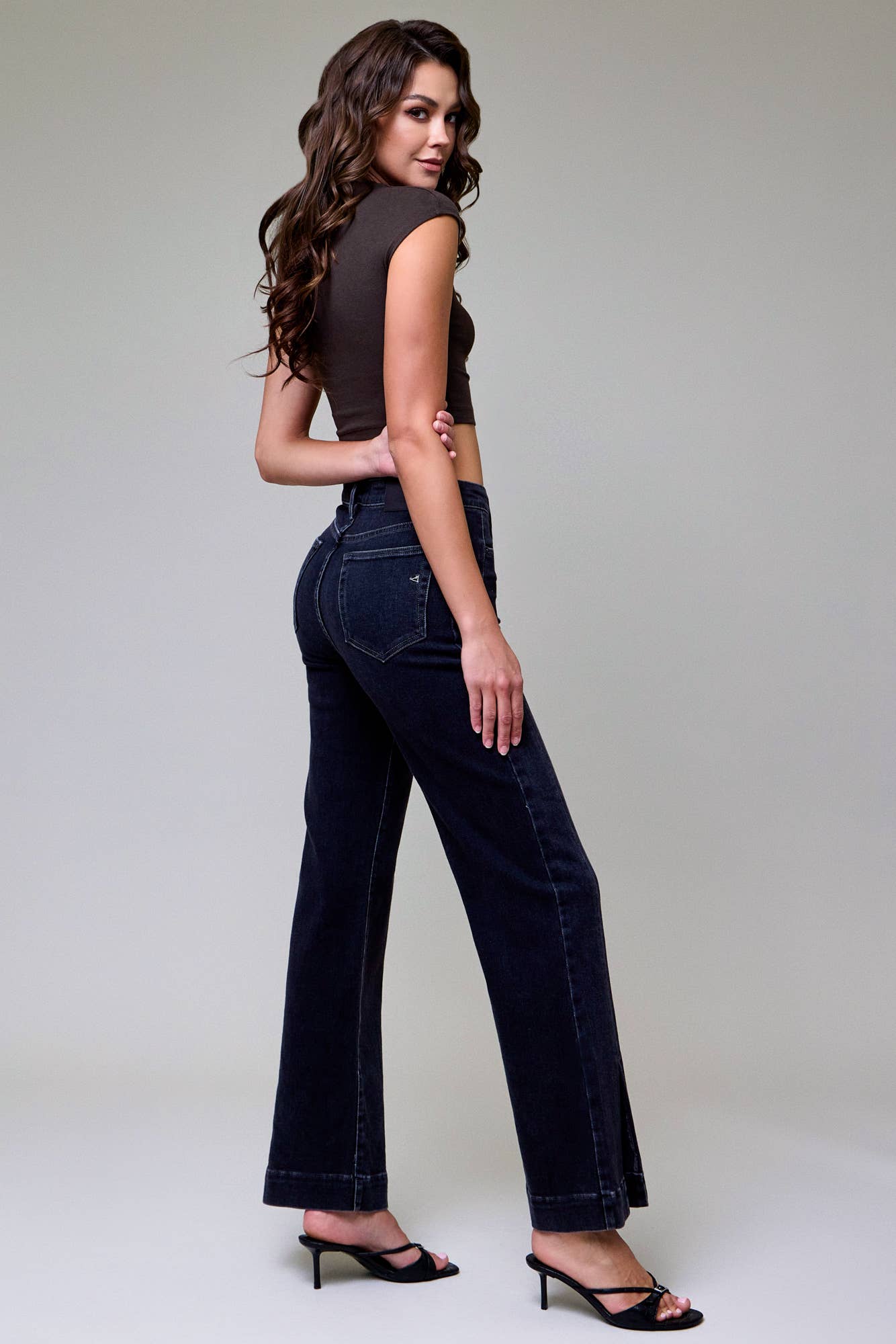 Woman wearing dark jeans and a black top on a plain background