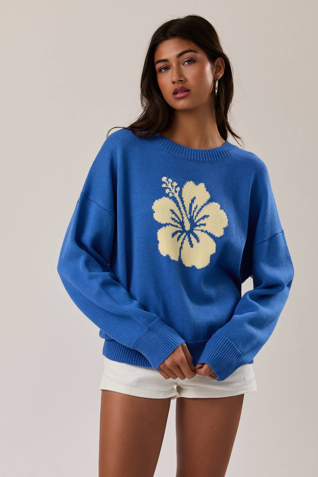 Woman wearing a blue sweater with a yellow floral design on a plain background
