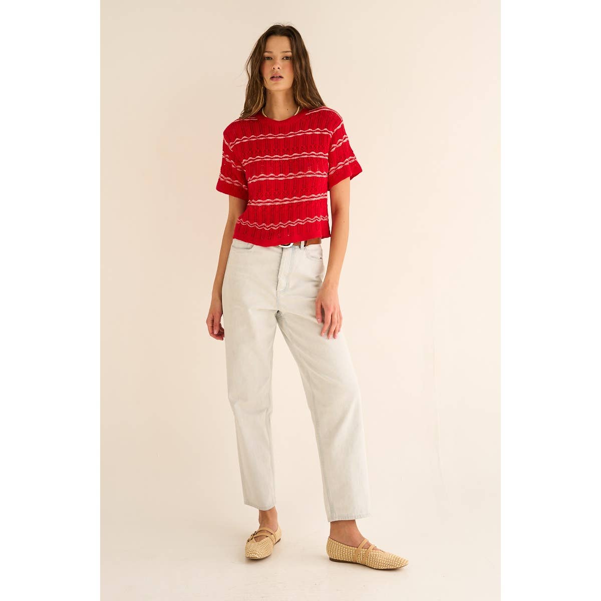 Woman wearing a red striped sweater and white pants on a beige background