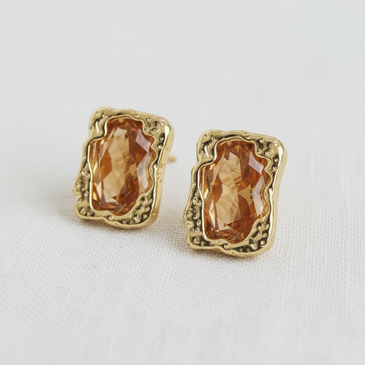 Angled view of brown faceted zircon stud earrings with textured gold-tone frames